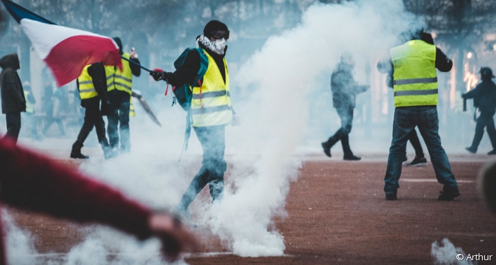 Manifestant gilet jaune brandissant un drapeau français au milieu des fumigènes