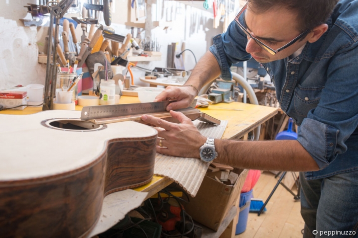 Un artisan luthier prend des mesures sur une guitare en cours de fabrication.