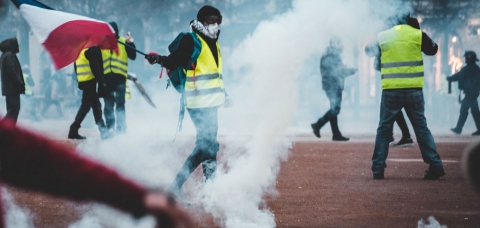 Manifestant gilet jaune brandissant un drapeau français au milieu des fumigènes