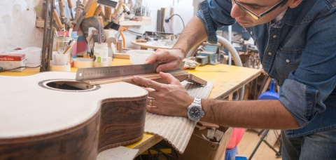 Un artisan luthier prend des mesures sur une guitare en cours de fabrication.